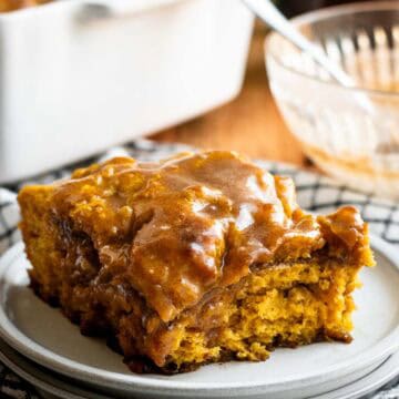 A square of pumpkin cinnamon roll focaccia with light brown glaze sitting on a grey plate.
