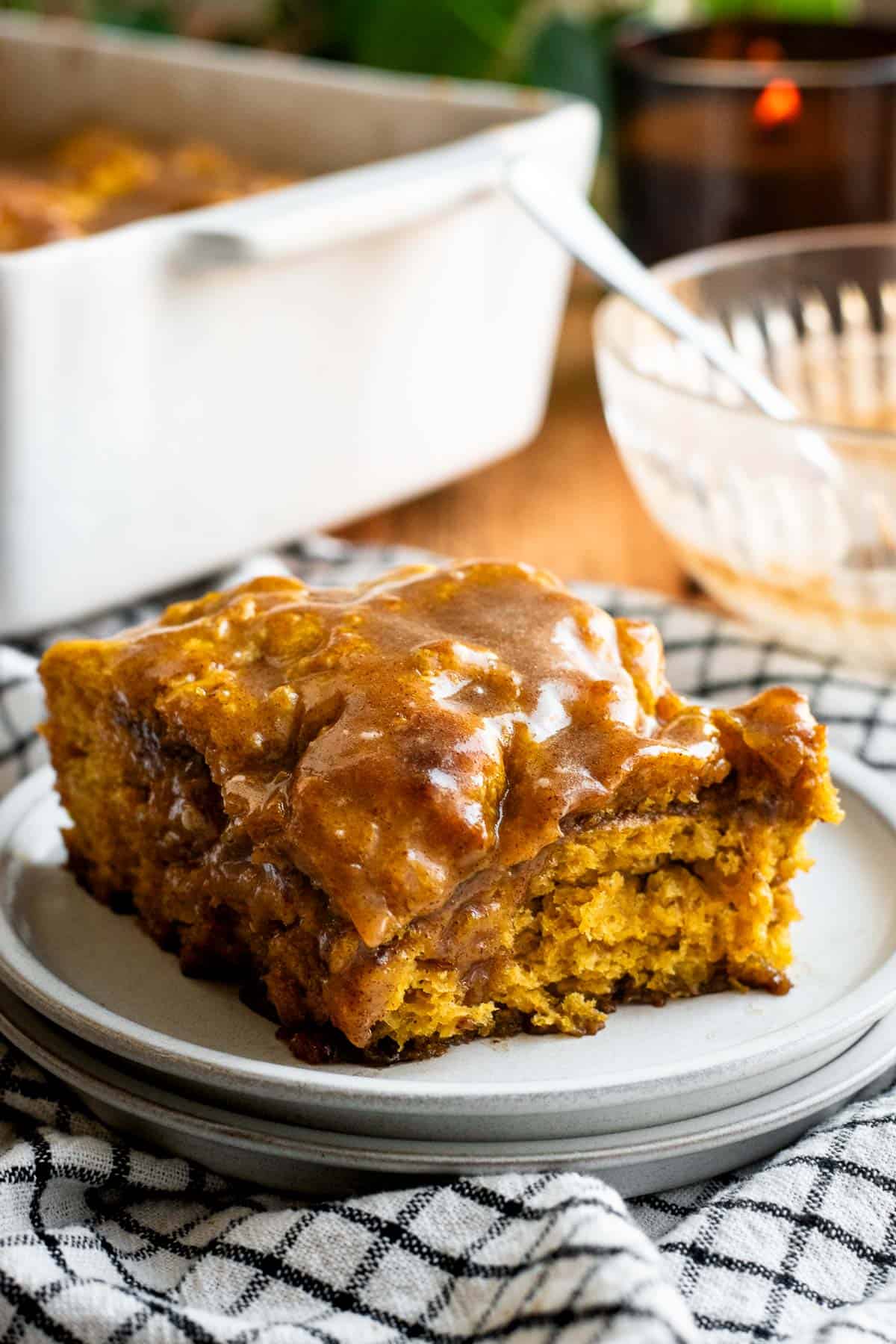 A square of pumpkin cinnamon roll focaccia with light brown glaze sitting on a grey plate. 