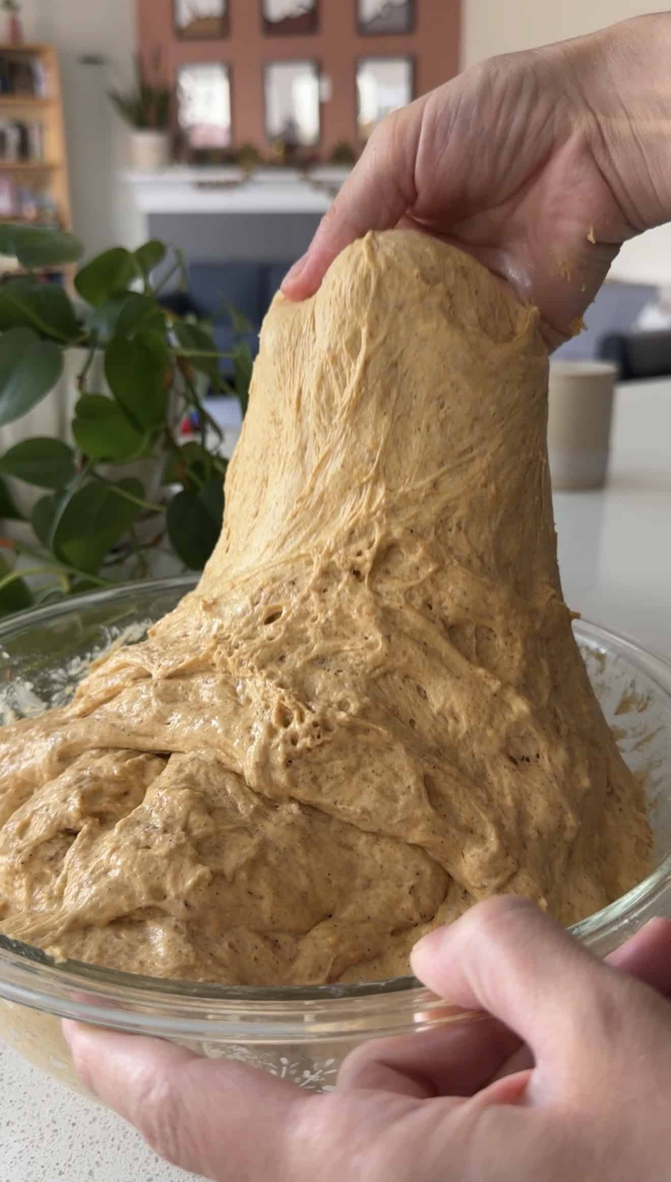 A hand stretching sticky focaccia bread dough out of a glass mixing bowl.