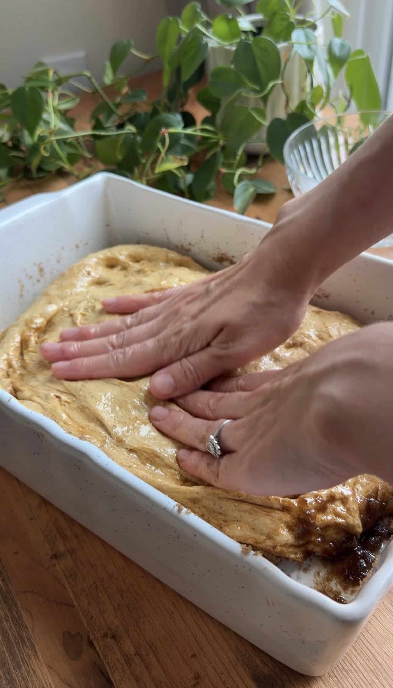 Two hands spreading pumpkin focaccia dough into a light baking dish.