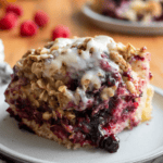 A large square of sweet focaccia filled with blueberries and raspberries and topped with oats and a white glaze sitting on a grey plate.