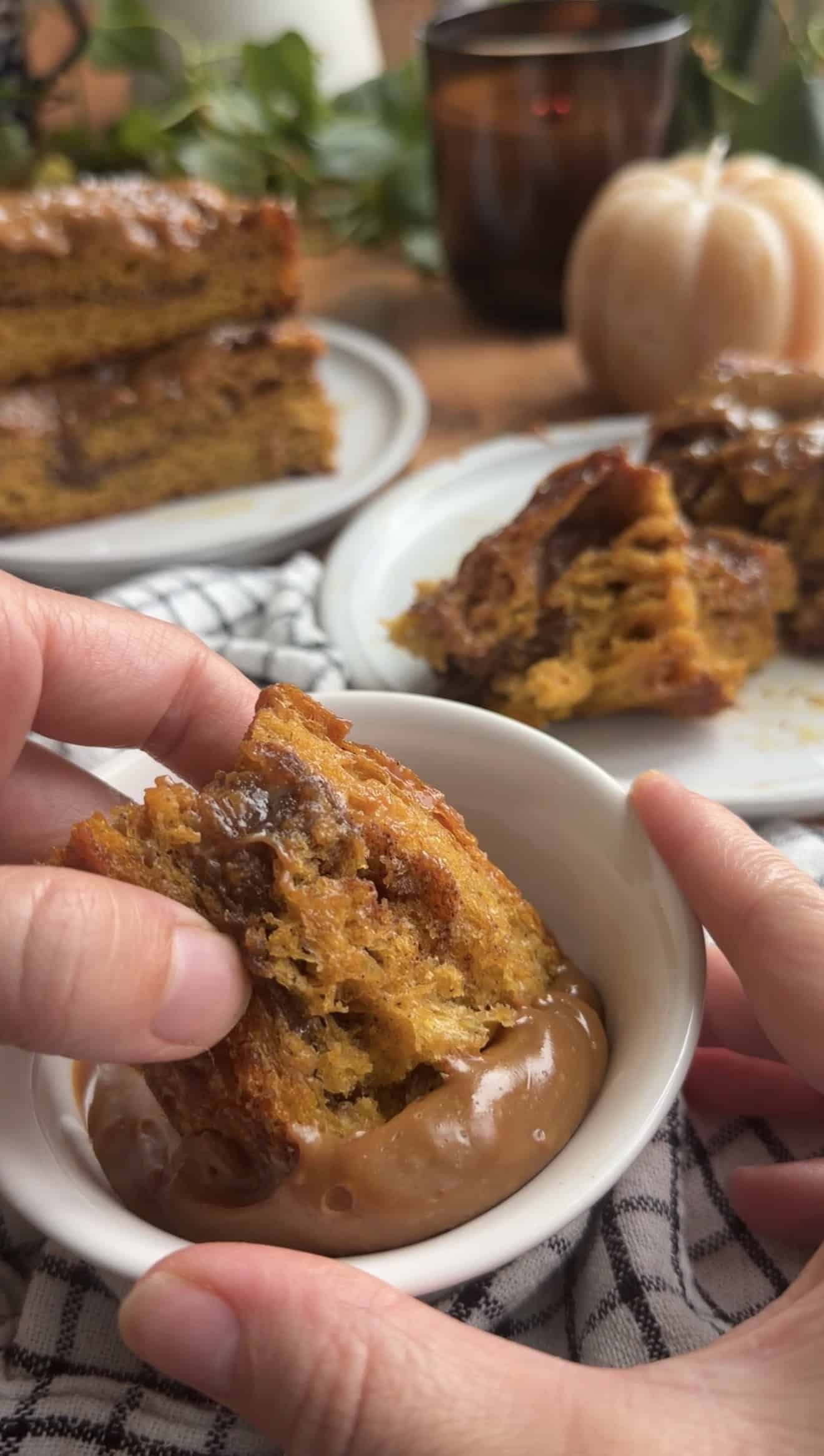 A hand dipping a torn piece of pumpkin churro focaccia into a small bowl of dulce de leche.