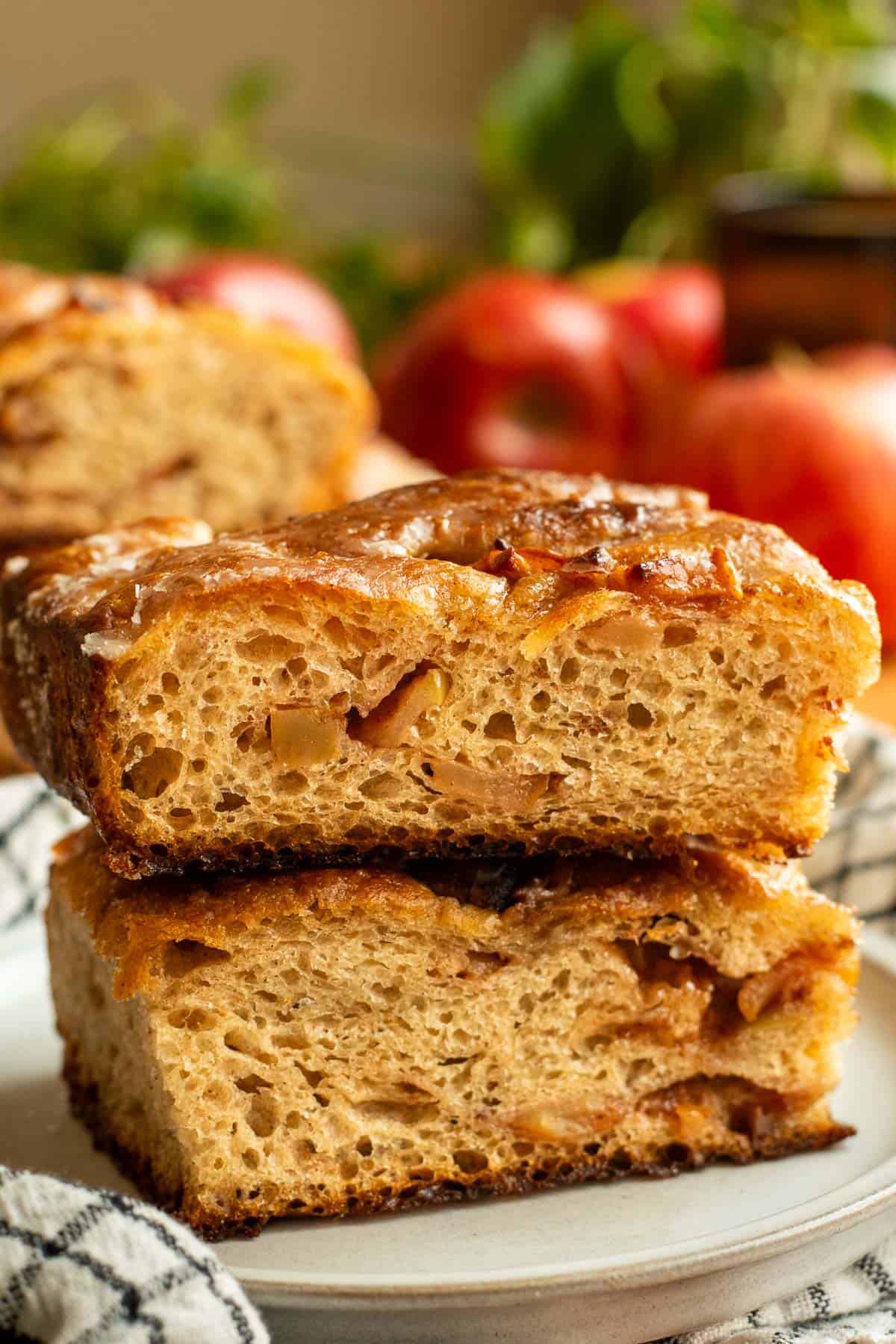 Two large pieces of apple fritter focaccia stacked on a small grey plate with whole apples in the background.