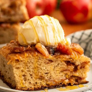 A large square of apple focaccia topped with a scoop of vanilla ice cream on a grey plate.