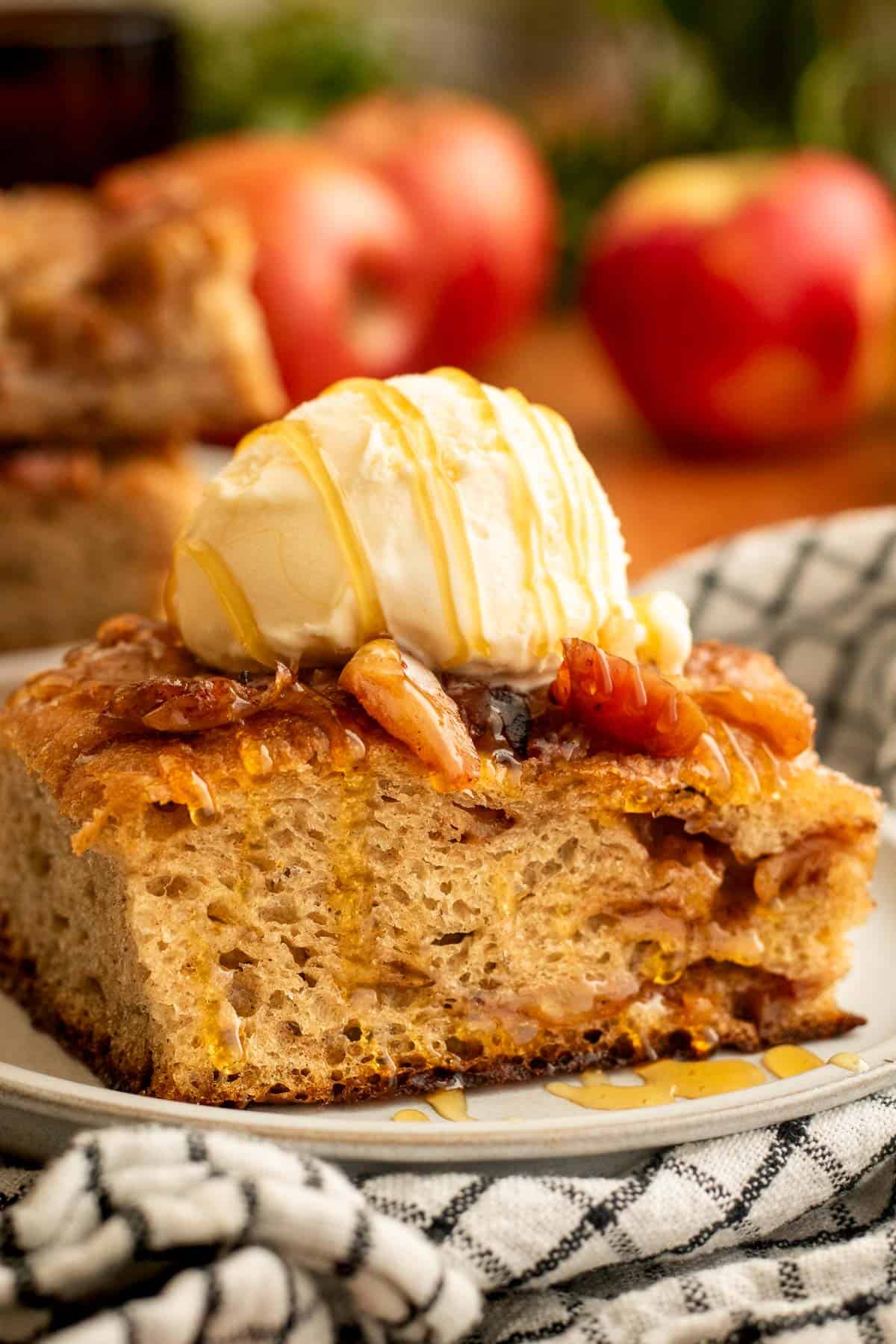 A large square of apple focaccia topped with a scoop of vanilla ice cream on a grey plate.