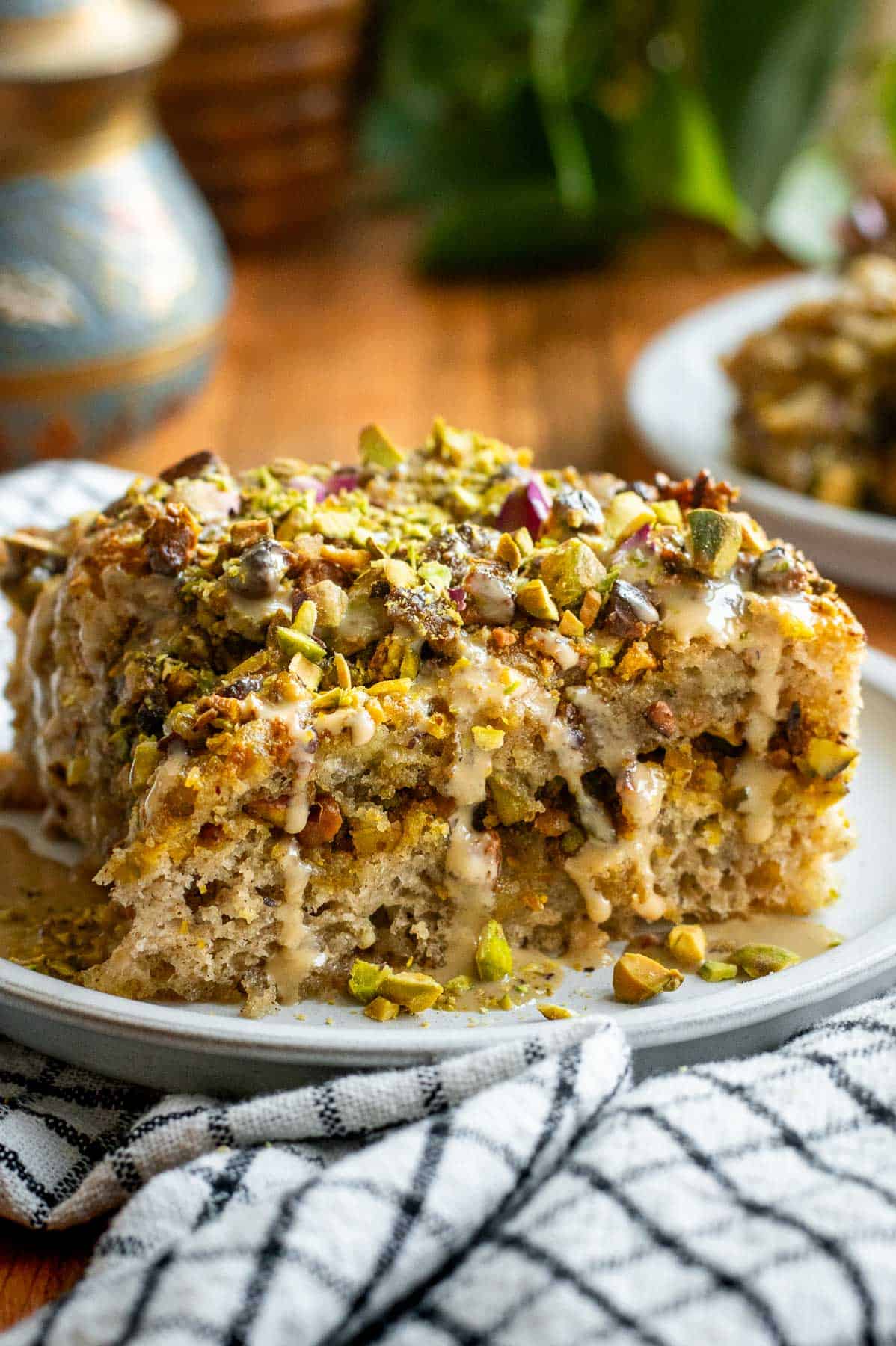 A large square of focaccia on a plate filled and topped with chopped pistachios as well as tahini and dried rose petals.