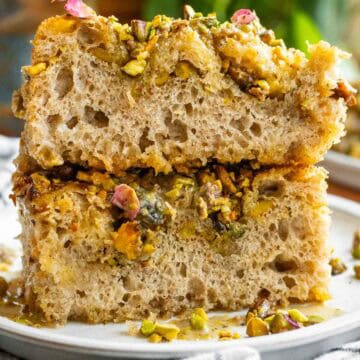 Two large slices of fluffy, airy focaccia topped with crushed pistachios, syrup, and dried rose petals.