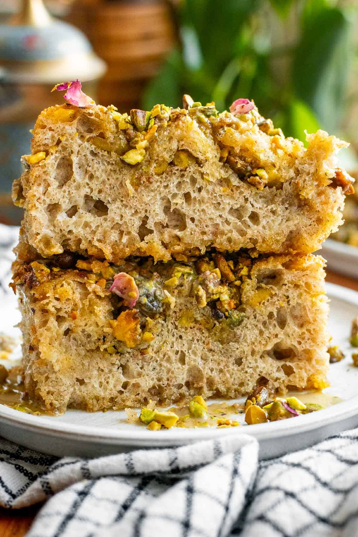Two large slices of fluffy, airy focaccia topped with crushed pistachios, syrup, and dried rose petals. 