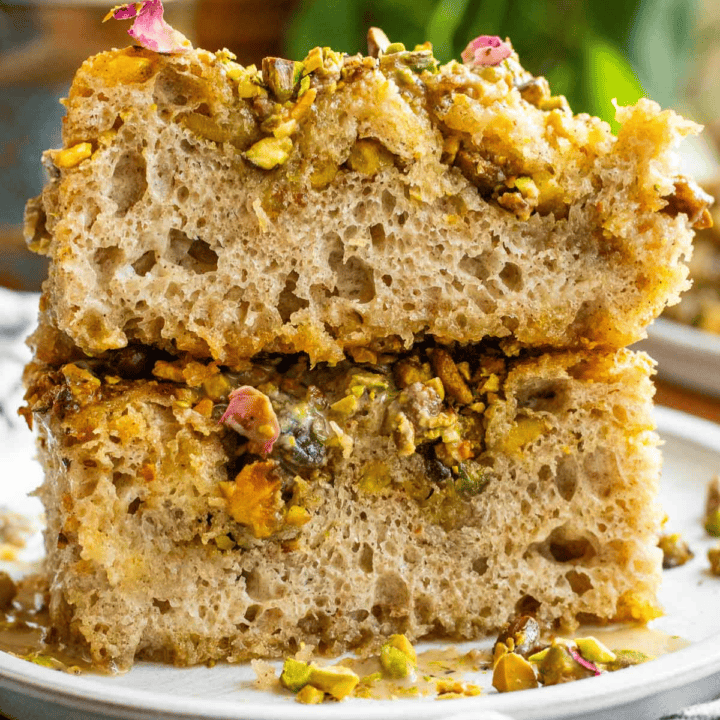 Two large pieces of fluffy focaccia topped with chopped pistachios and dried rose petals on a grey plate.