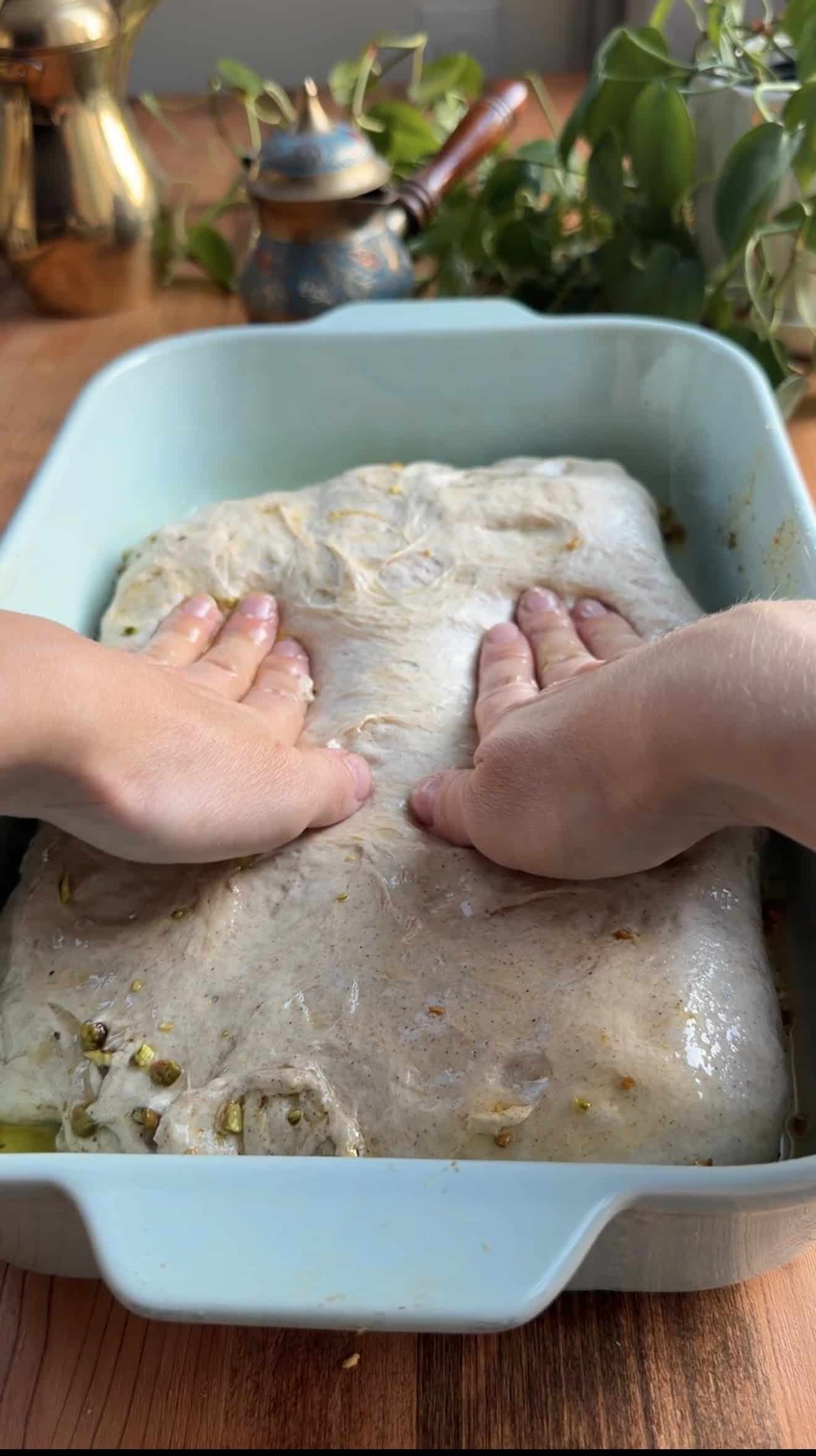 Two hands spreading focaccia dough into a blue baking dish.