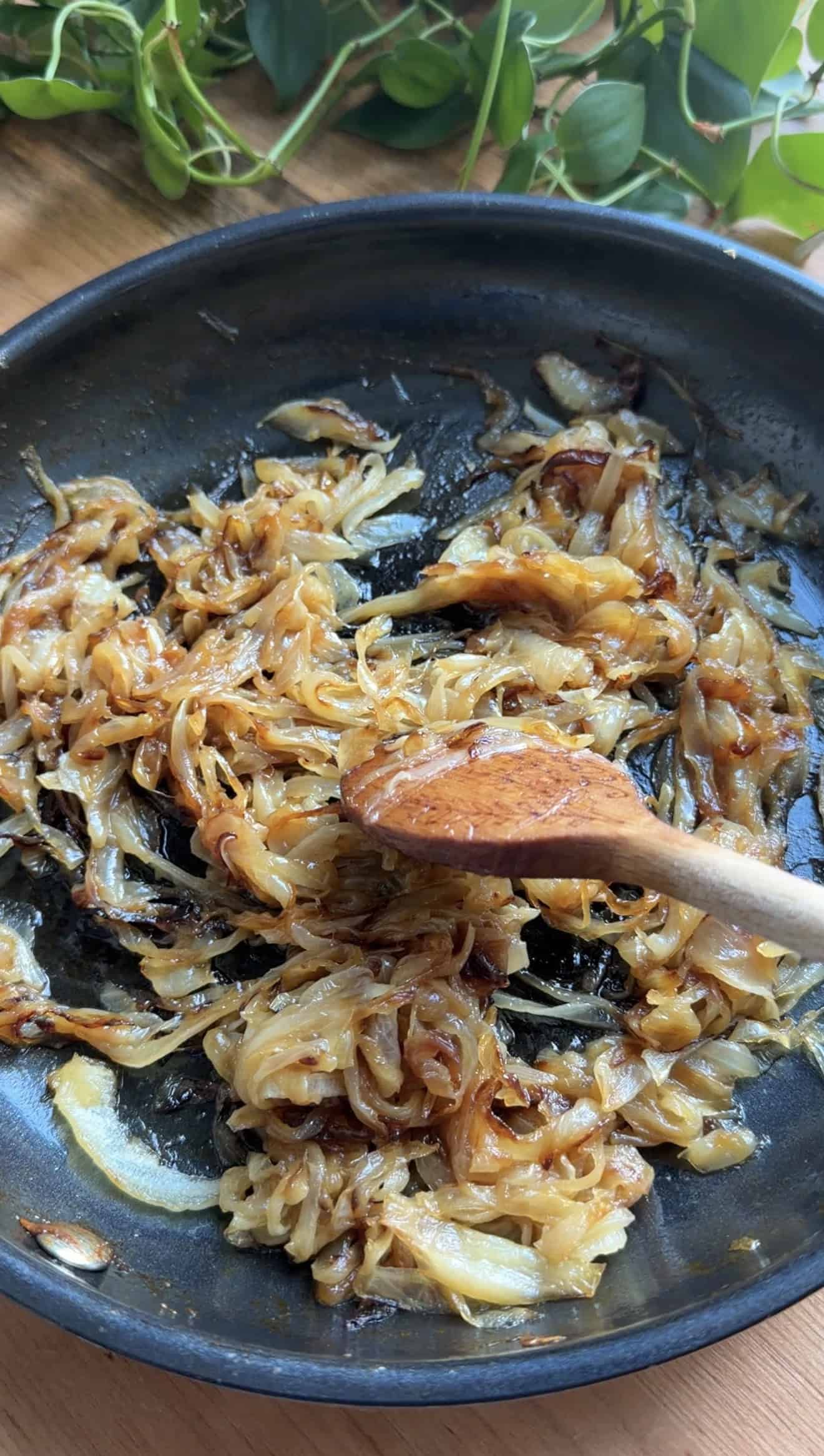 A wooden spoon stirring caramelized onions in a saucepan.