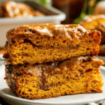 Two large pieces of cinnamon-swirled focaccia topped with cinnamon sugar and caramel glaze stacked on a small plate.