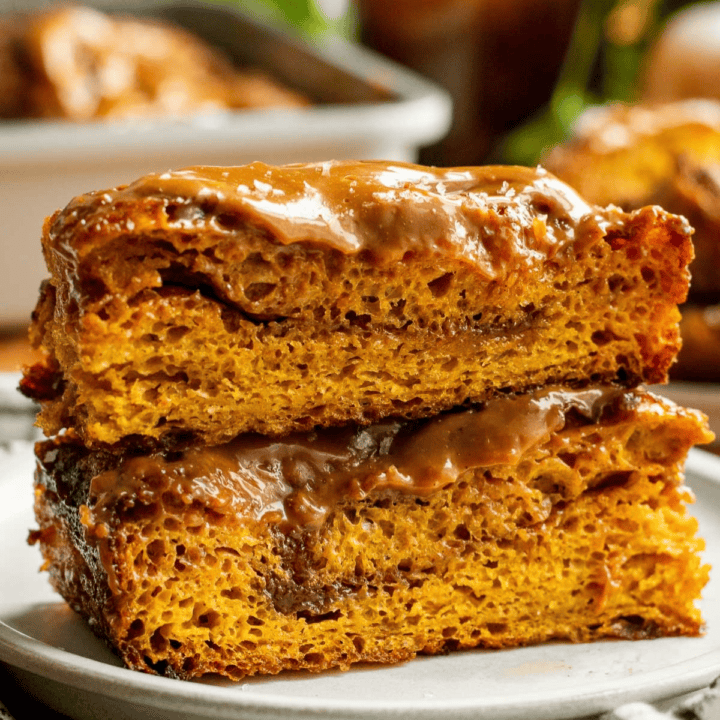 Two large pieces of cinnamon-swirled focaccia topped with cinnamon sugar and caramel glaze stacked on a small plate.