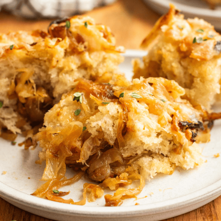 Three slices of focaccia bread on a plate filled and topped with caramelized onions and melted cheese.