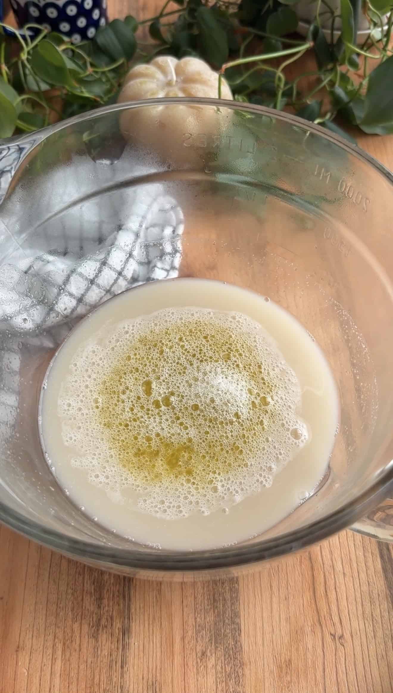A mixing bowl filled with frothy, activated yeast in water and olive oil.
