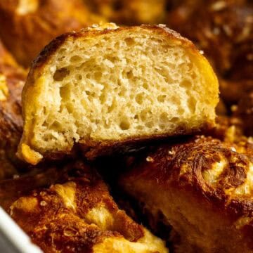 A fluffy piece of pretzel focaccia sitting on the rest of the baked bread in a white casserole dish.