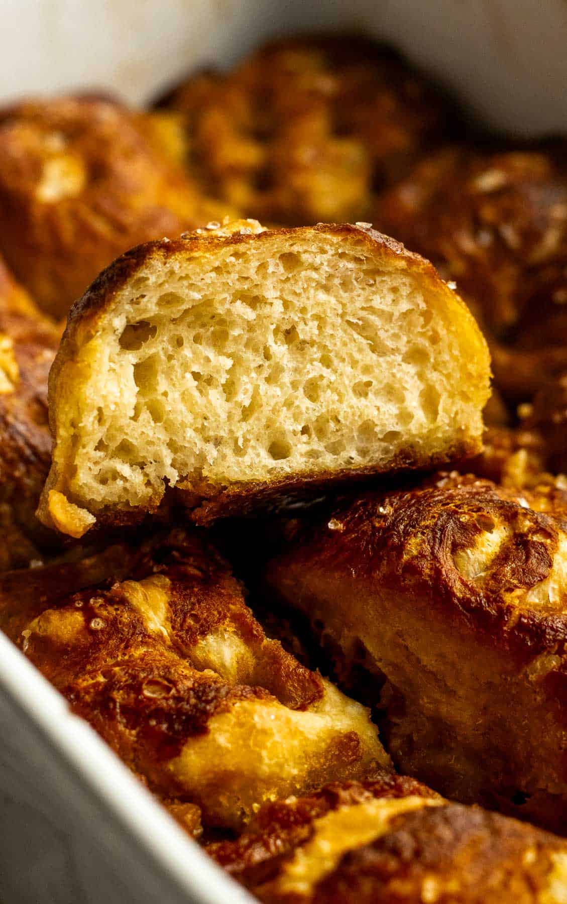 A fluffy piece of pretzel focaccia sitting on the rest of the baked bread in a white casserole dish. 