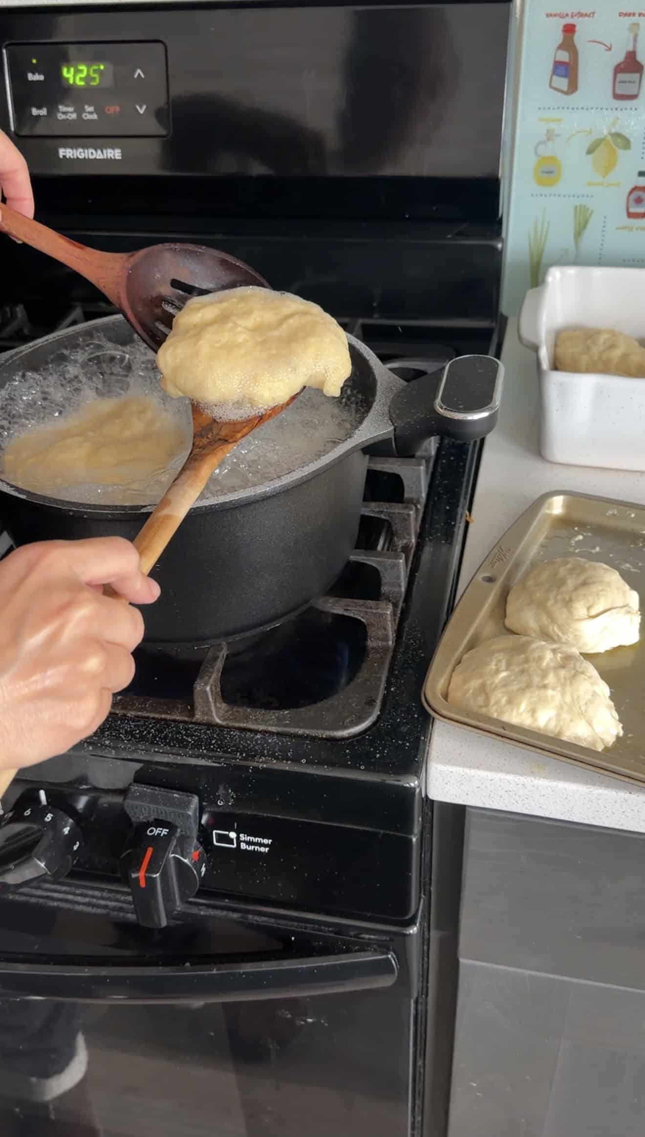 Two hands lifting a boiled ball of focaccia dough out of a pot on the stove with two wooden spoons.