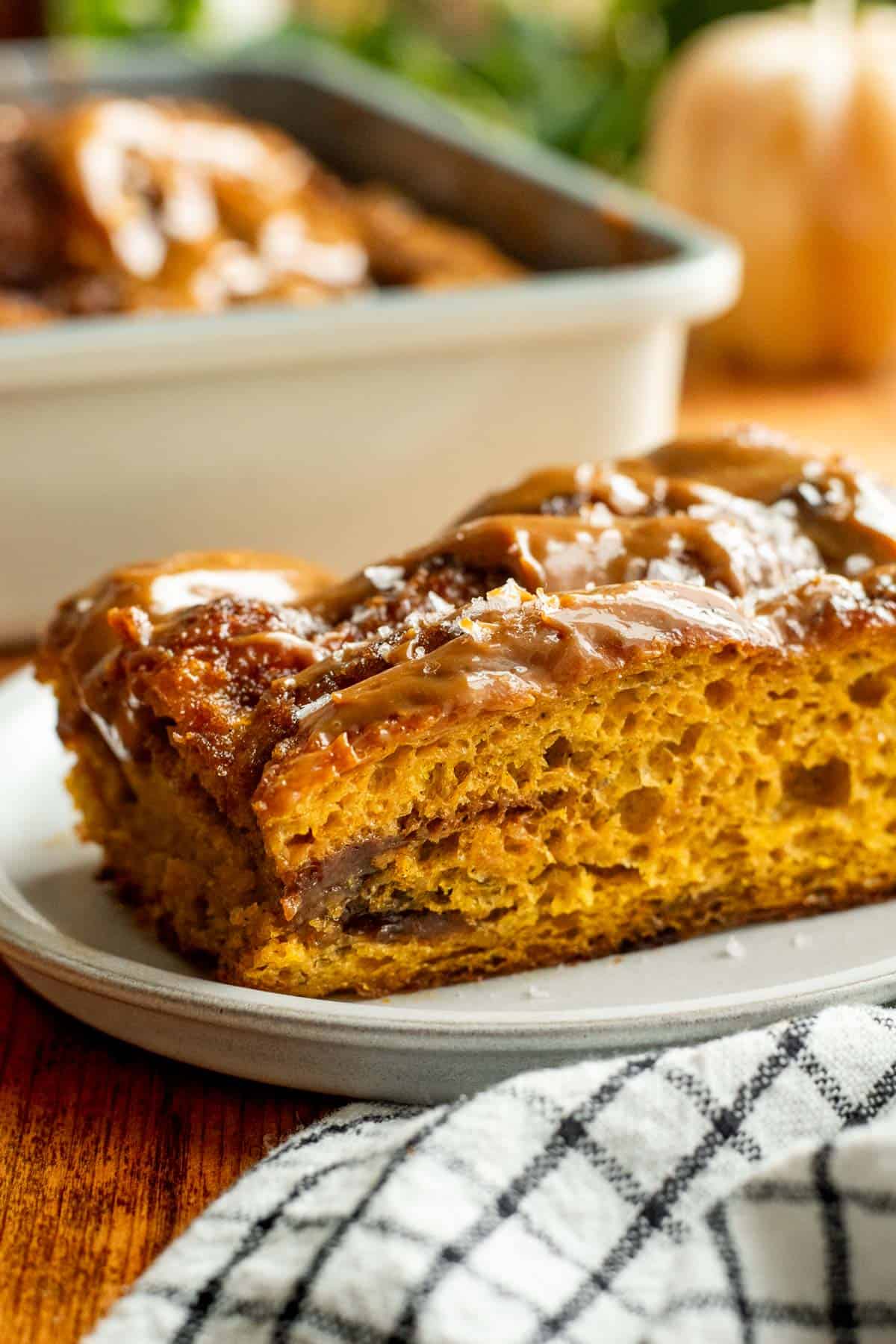 A piece of fluffy orange focaccia on a grey plate with a cinnamon sugar swirl in the middle and dulce de leche glaze on top.