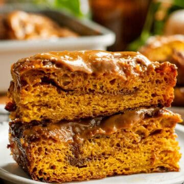 Two large squares of cinnamon-filled pumpkin focaccia stacked on top of each other topped with caramel glaze.