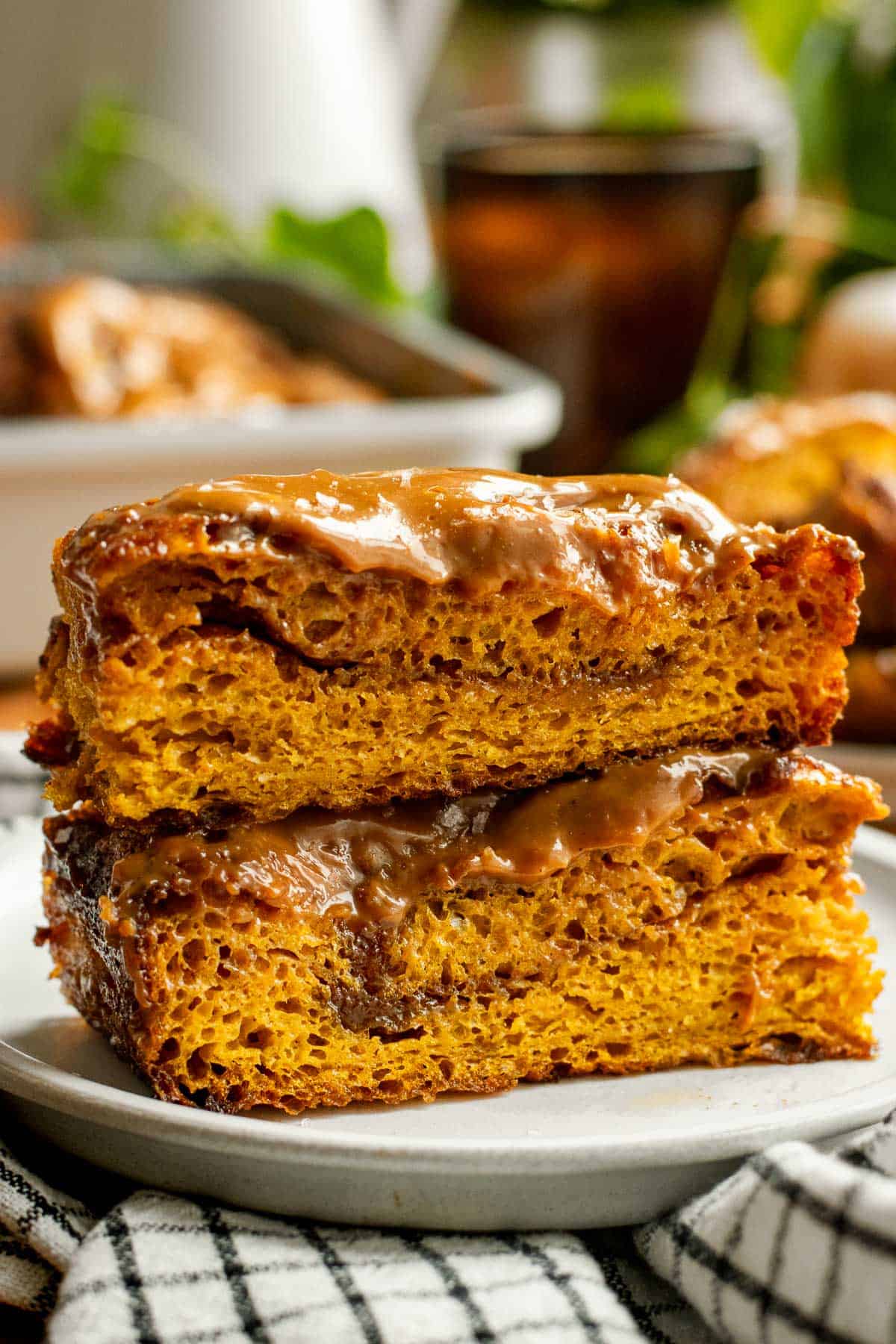 Two large squares of cinnamon-filled pumpkin focaccia stacked on top of each other topped with caramel glaze.
