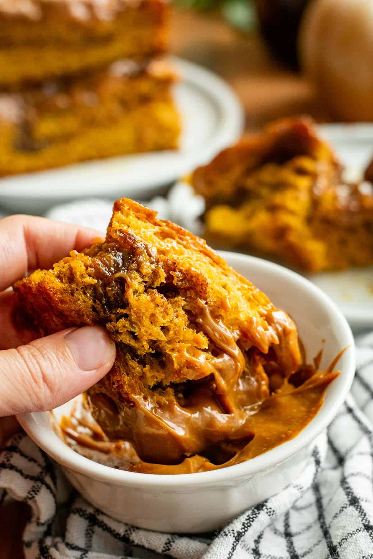 A hand dipping a piece of pumpkin churro focaccia into a small bowl of dulce de leche.