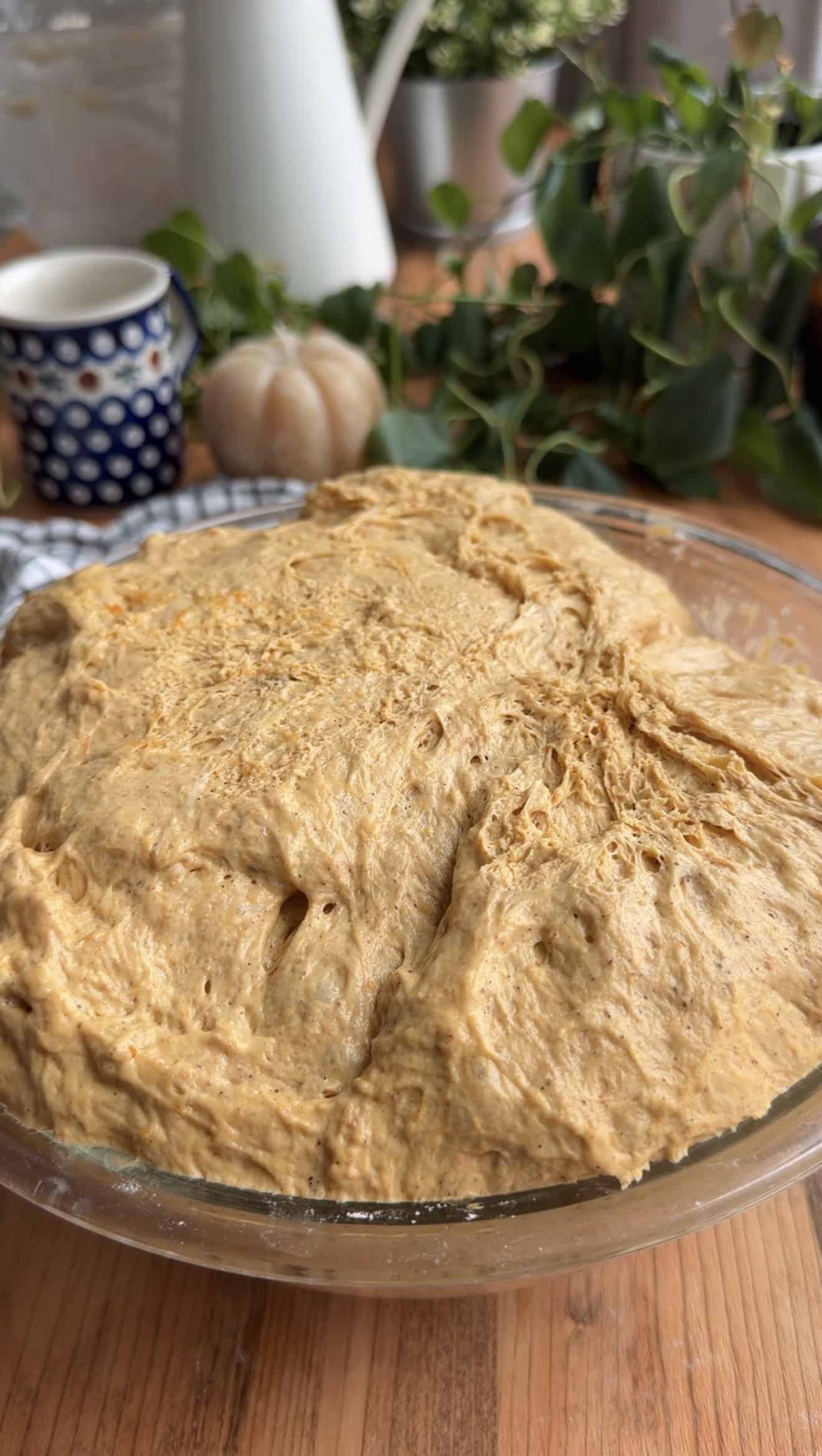 A glass bowl with bubbly, risen pumpkin focaccia in it.