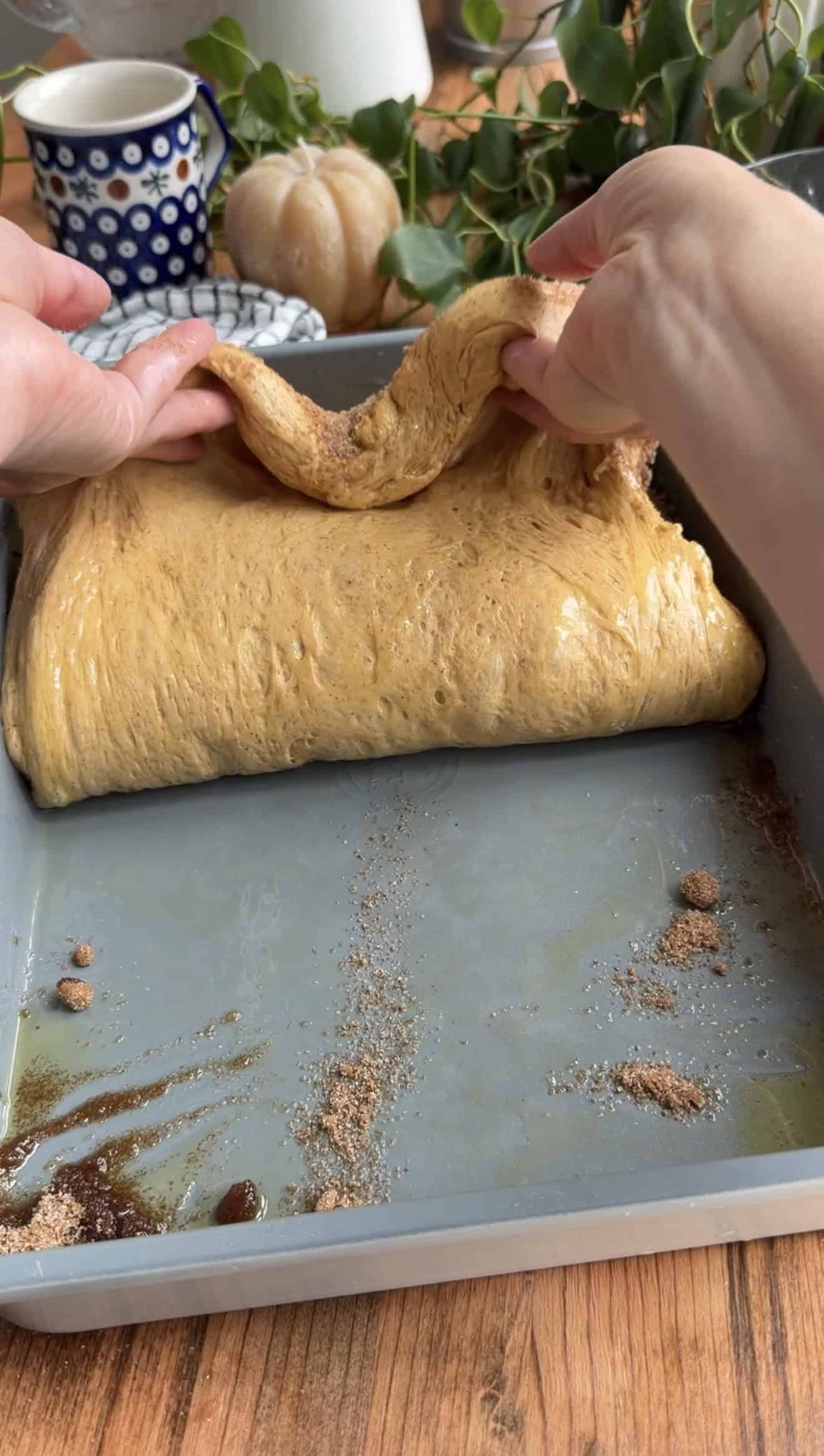 Two hands folding orange pumpkin focaccia in half with cinnamon sugar inside.
