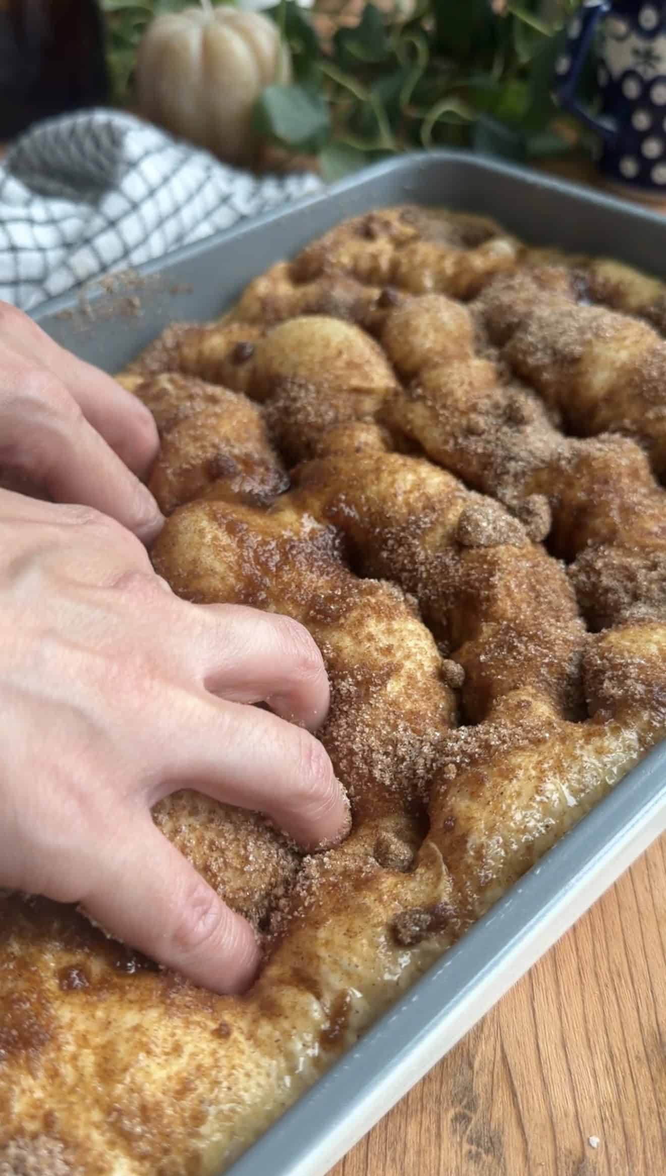 Two hands dimpling cinnamon and sugar coated focaccia dough in a metal baking dish.