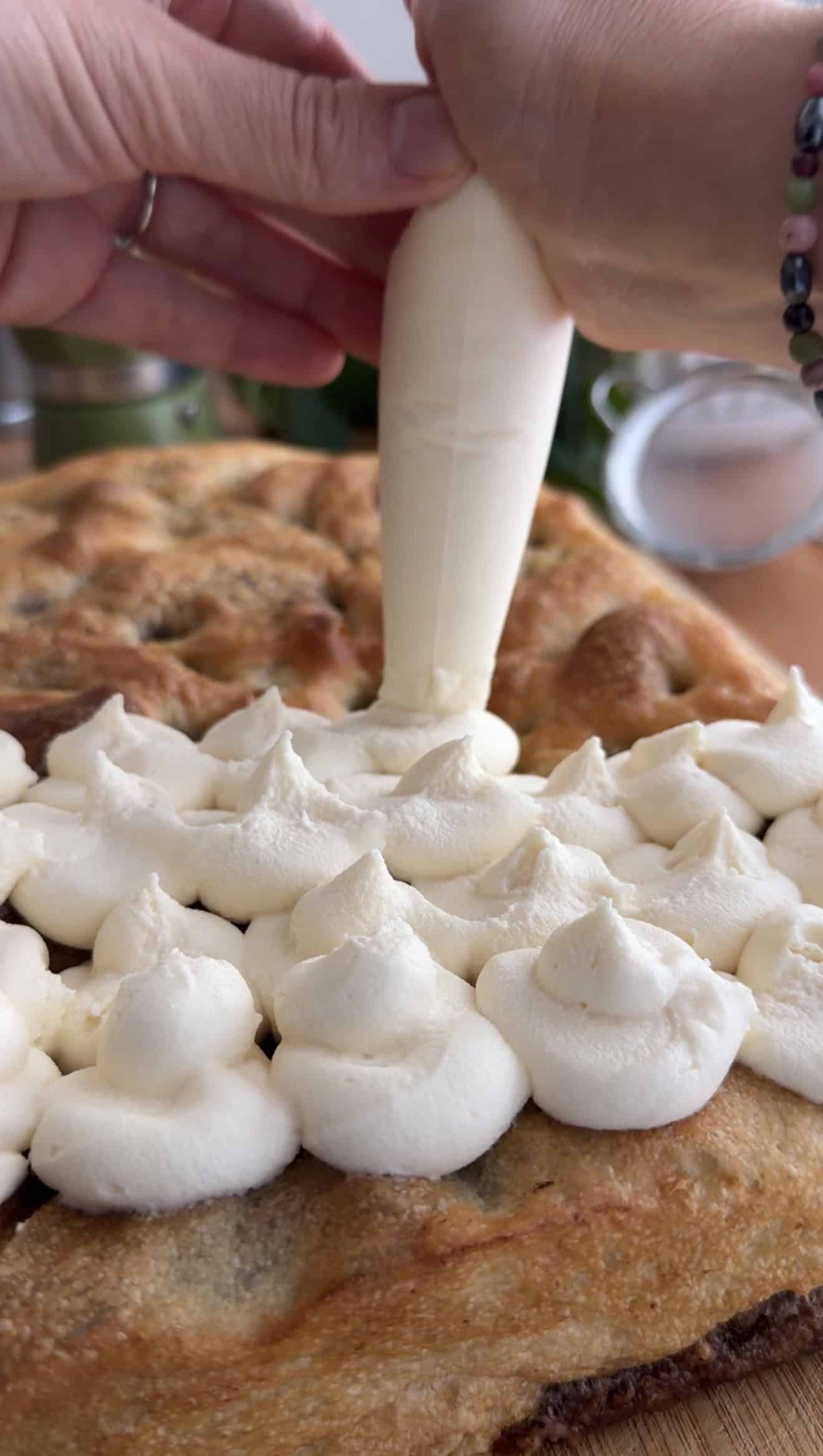 Two hands piping whipped mascarpone onto baked focaccia in little dollops.