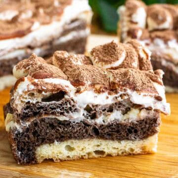 A large piece of white and black marbled focaccia topped with whipped mascarpone and cocoa powder on a wooden board.