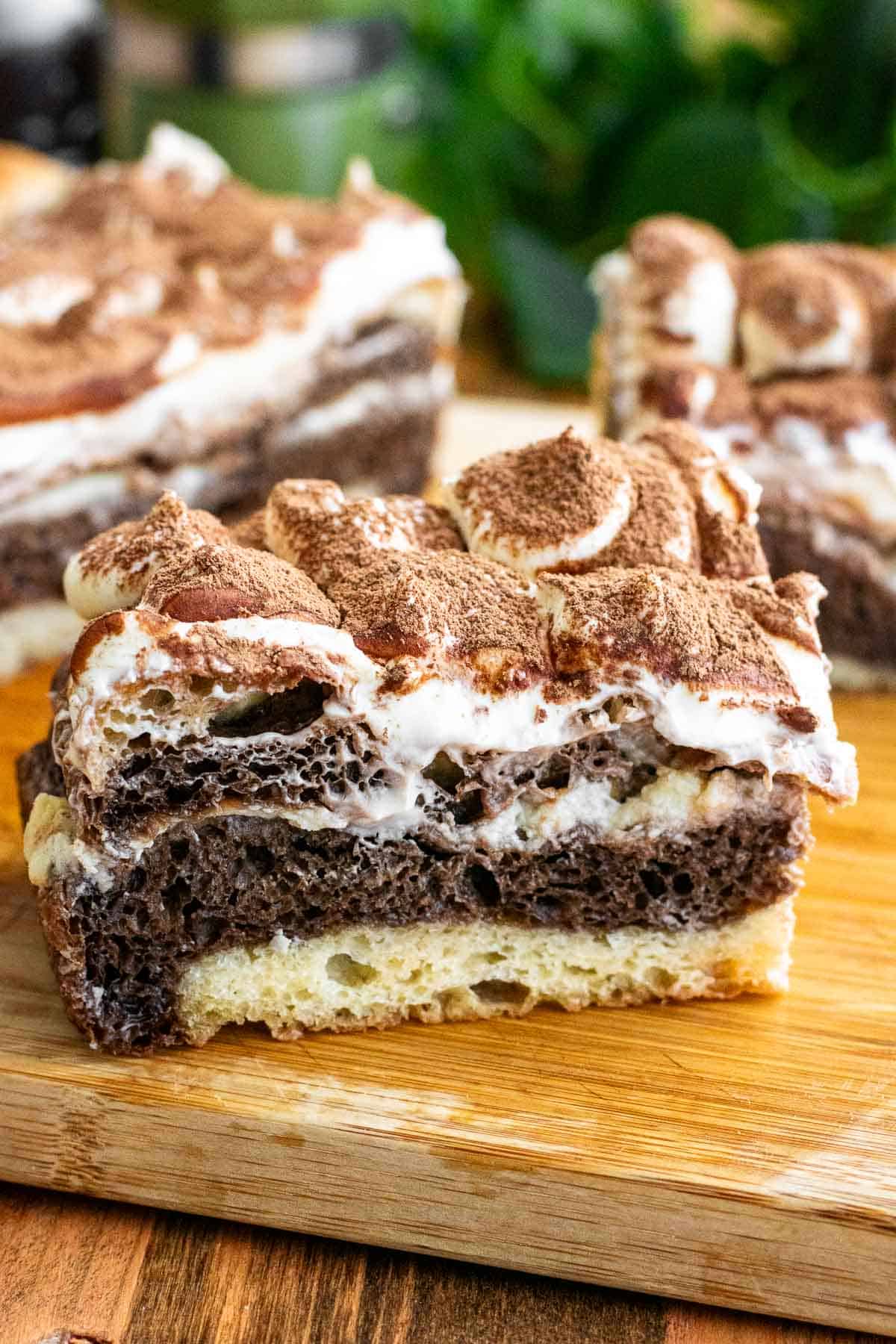 A large piece of white and black marbled focaccia topped with whipped mascarpone and cocoa powder on a wooden board.