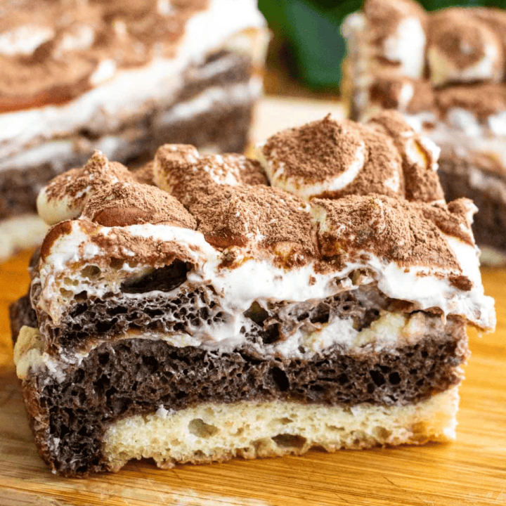 A piece of black and white marbled focaccia bread topped with whipped cream cheese and sifted cocoa powder sitting on a wooden board.