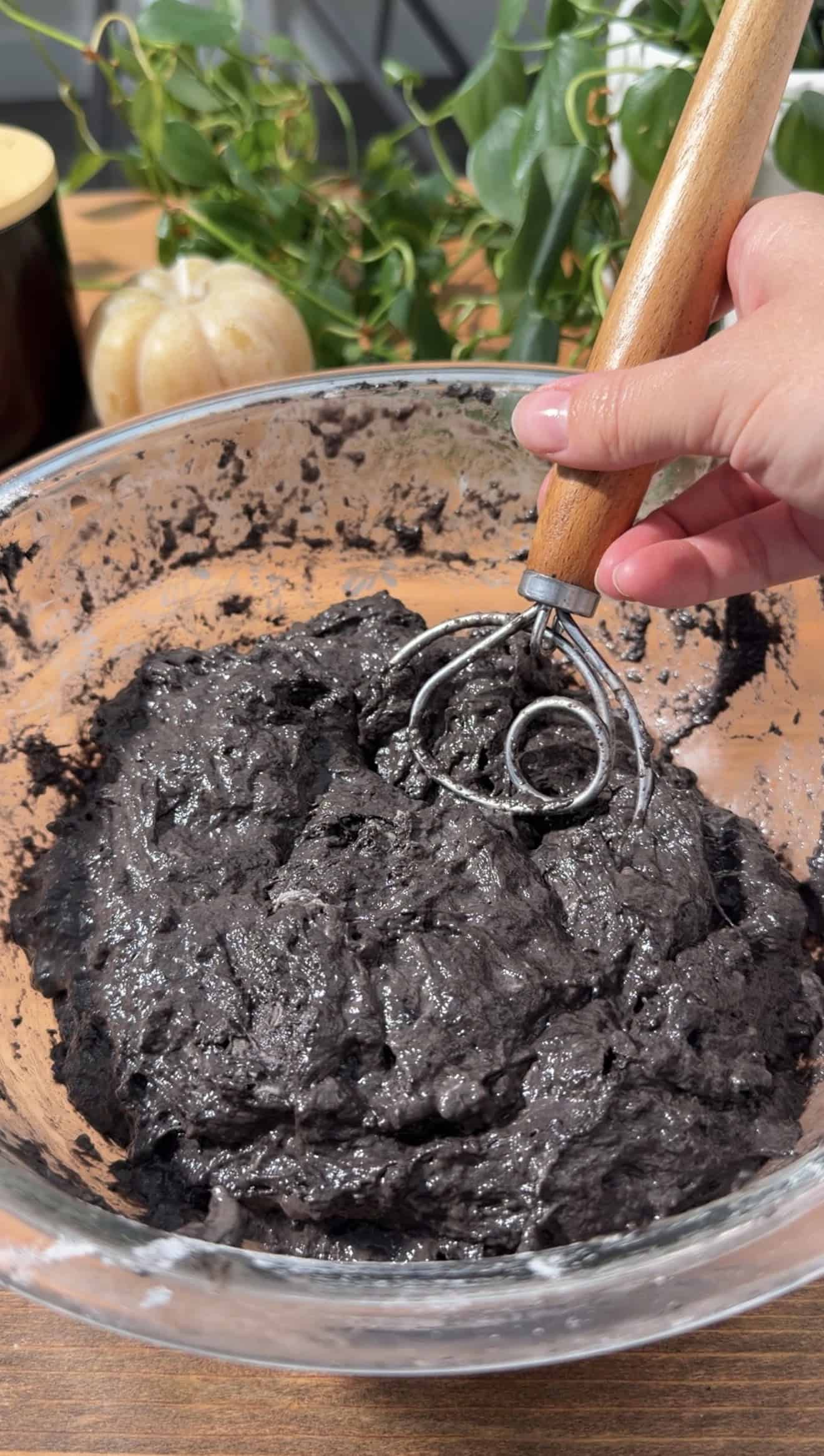 A hand stirring black bread dough with a Danish dough whisk.