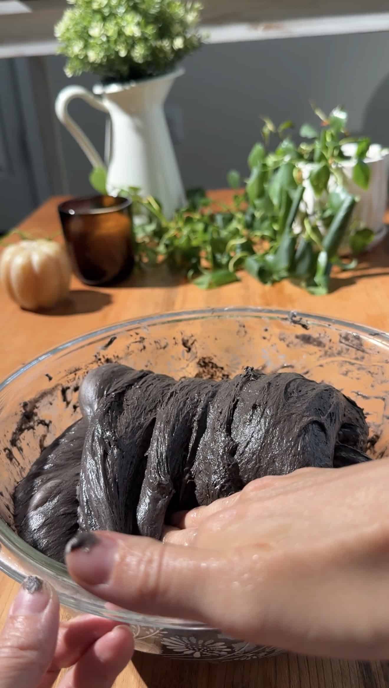 A hand folding black bread dough over itself in a mixing bowl.
