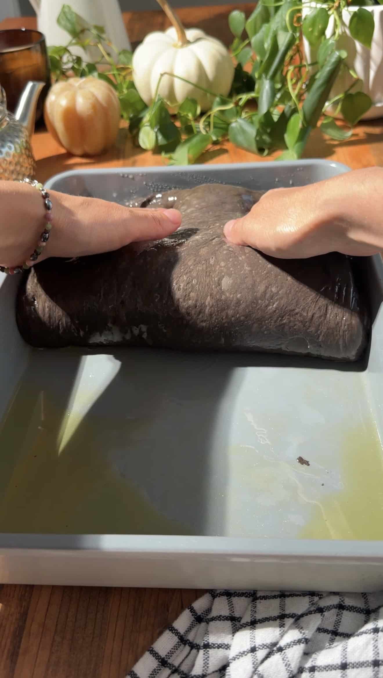 Two hands folding focaccia dough in an oiled metal baking dish.