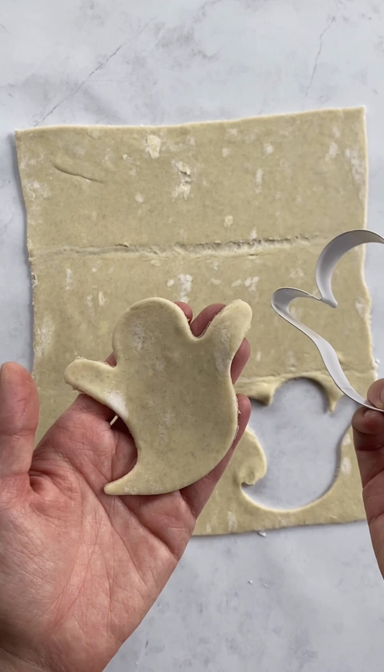 A hand holding a ghost-shaped piece of cut-out puff pastry dough.