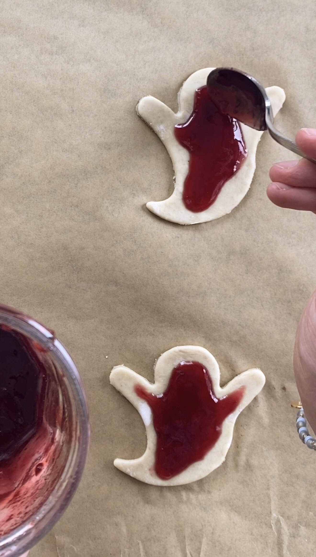 A hand spreading red jam onto puff pastry with a spoon.