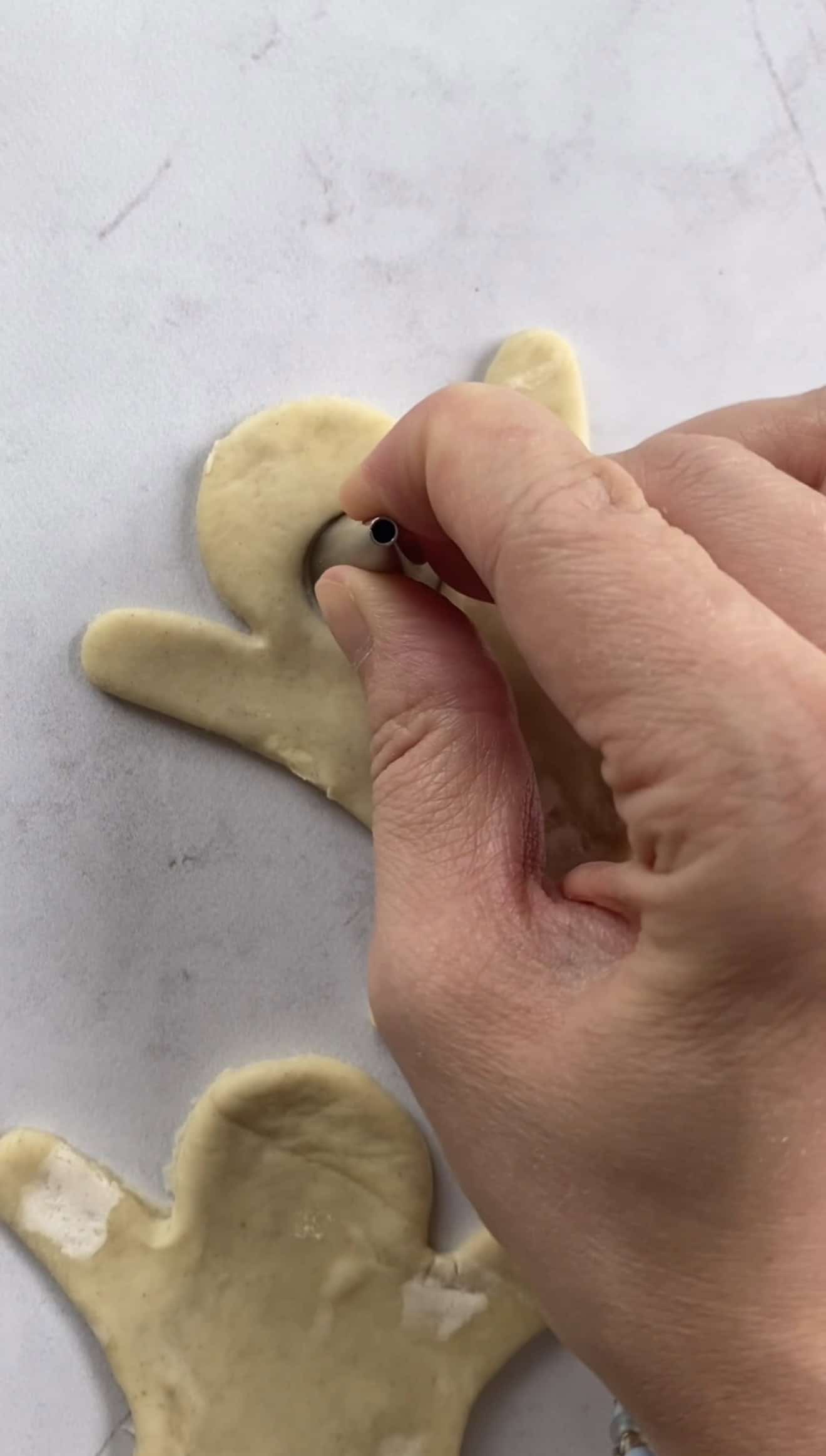 A hand cutting out a mouth from a ghost-shaped puff pastry with a metal piping nozzle.