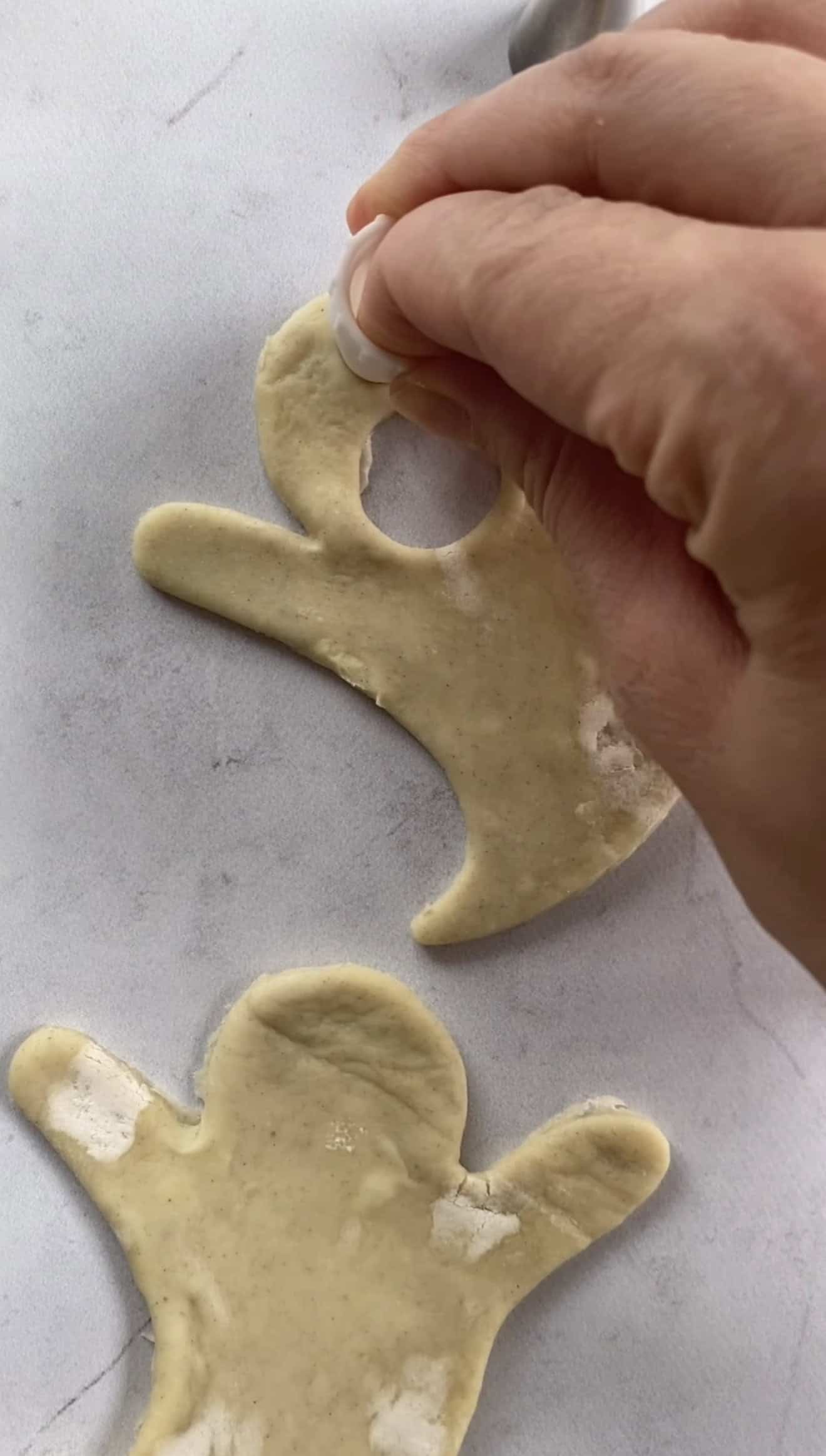 A hand cutting out eyes from a ghost-shaped pastry dough with a piping nozzle.