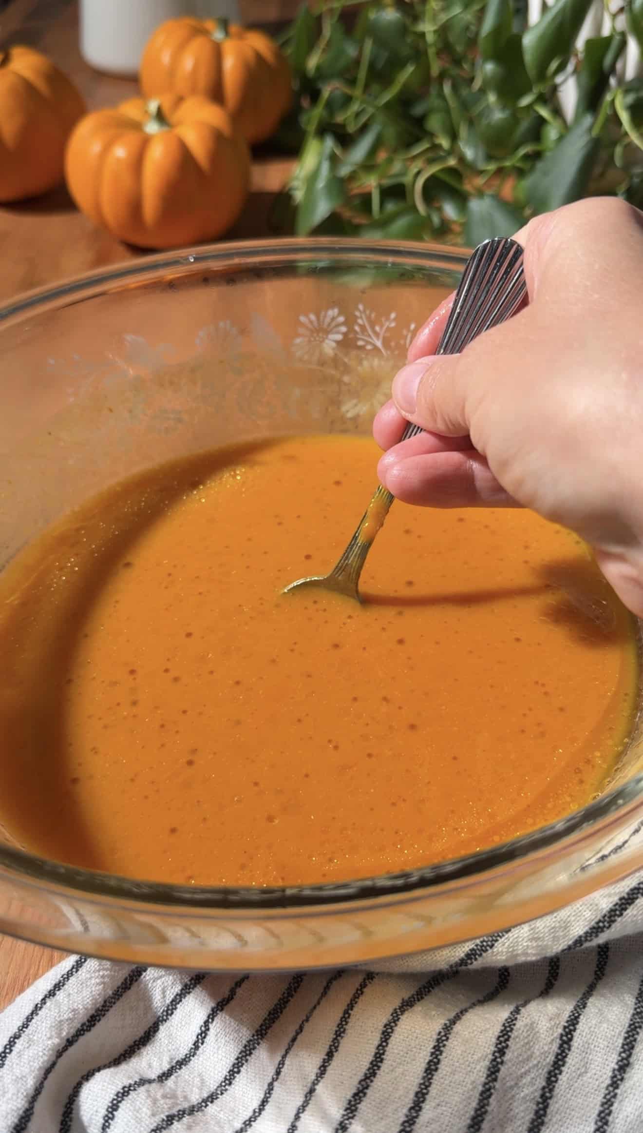A hand stirring a bright orange liquid in a glass mixing bowl.