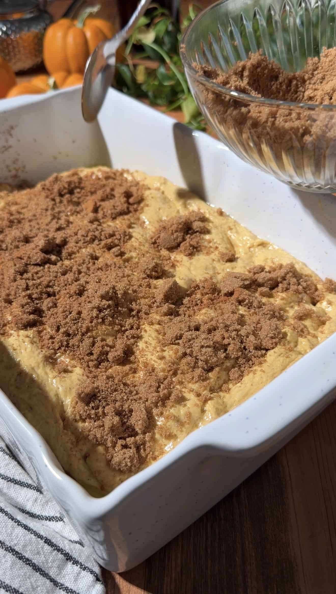 A spoon sprinkling brown sugar and cinnamon onto orange focaccia dough in a baking dish.