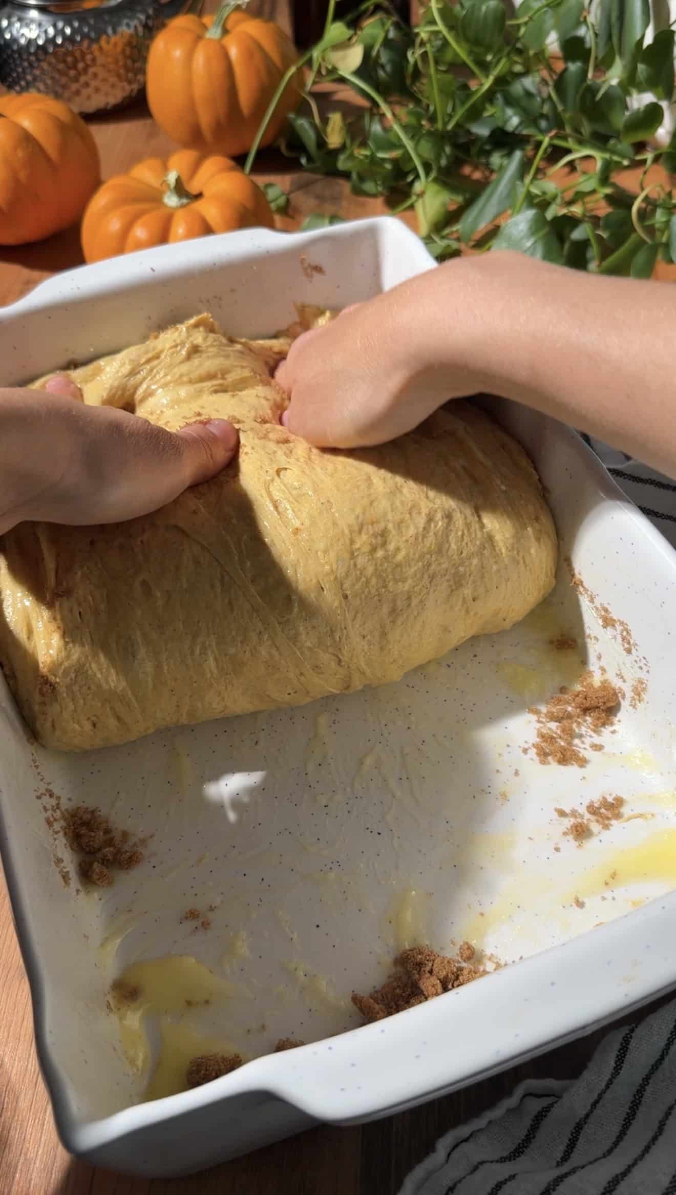 Two hands folding focaccia dough in half in a baking dish.