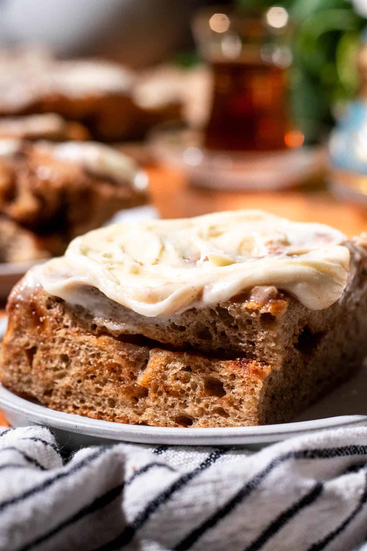 A large square of chai spiced focaccia topped with fluffy cream cheese frosting on a grey plate on a black and white linen.