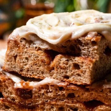 Two large pieces of chai focaccia with a cinnamon sugar filling stacked on top of each other and topped with cream cheese frosting.