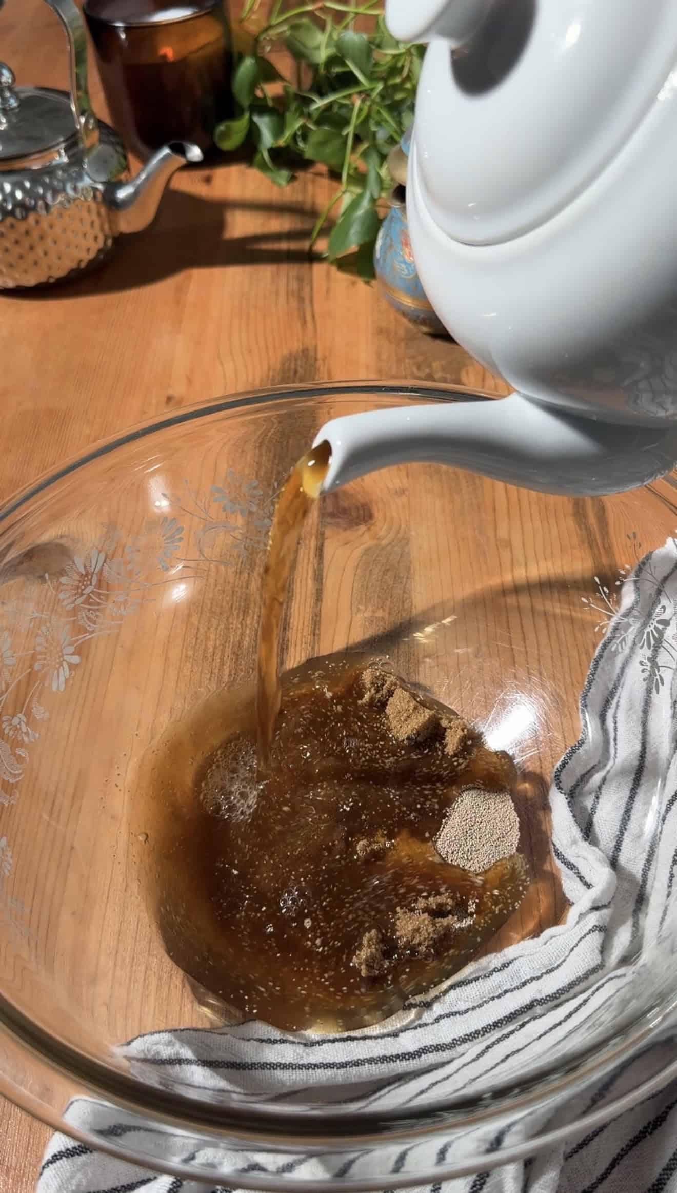 Tea pouring from a white kettle into a glass mixing bowl.