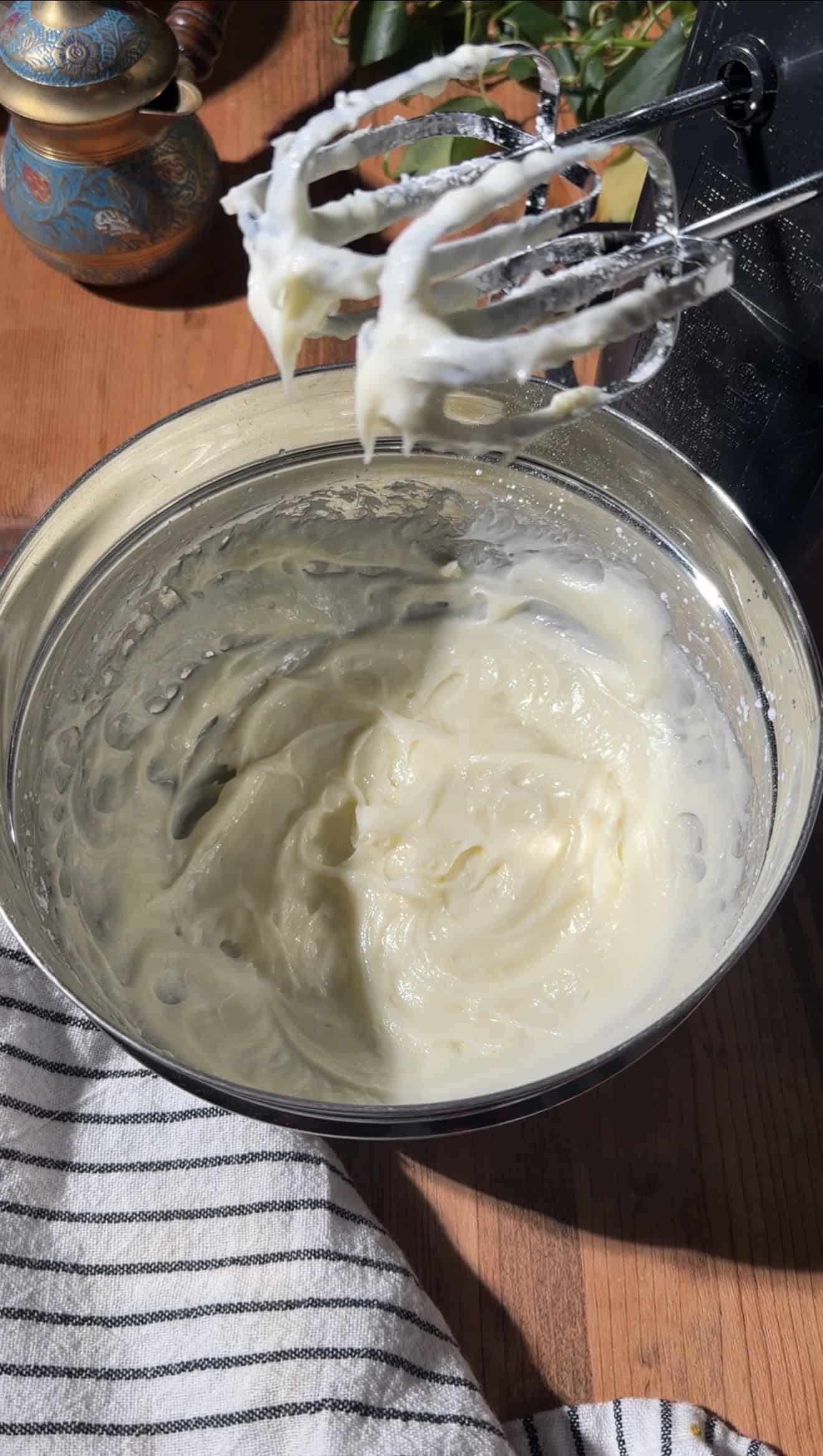 Fluffy cream cheese frosting in a metal mixing bowl on a table next to a hand mixer.