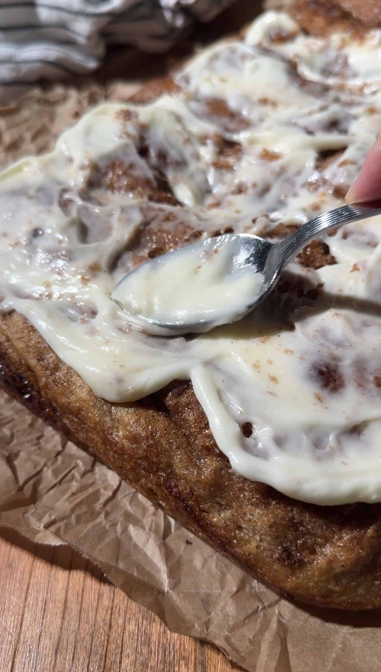 A metal spoon spreading fluffy cream cheese frosting onto baked focaccia.