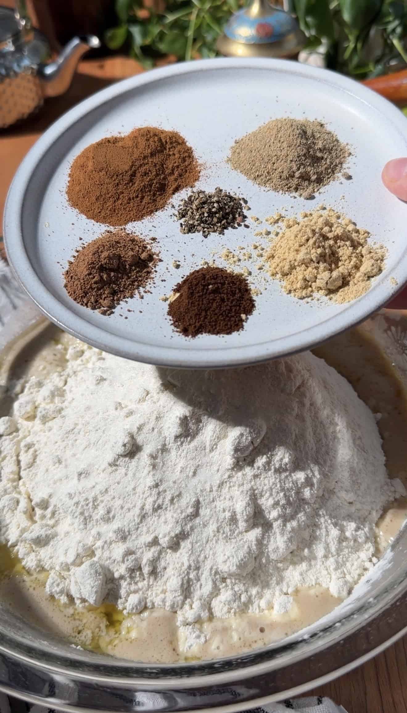 A place with six small piles of baking spices held over a mixing bowl with flour.
