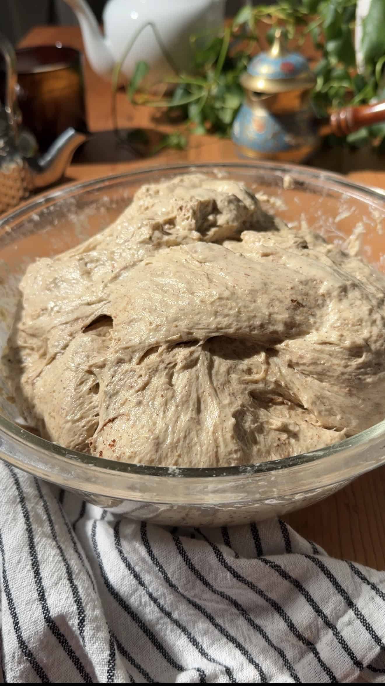 Spiced focaccia dough in a glass mixing bowl on a table next to a black and white linen.